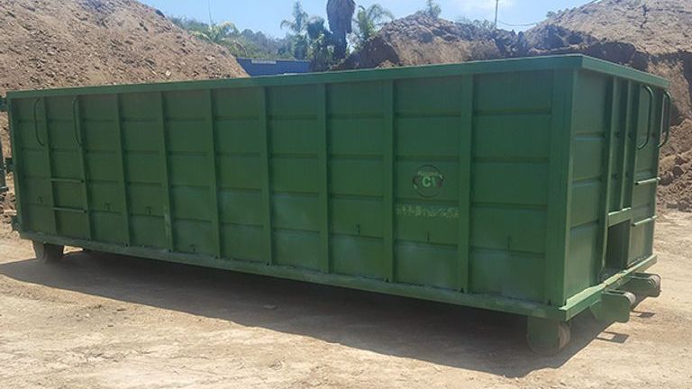 A large green dumpster is sitting on top of a dirt field.