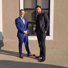 Two men in suits are standing next to each other in front of a window