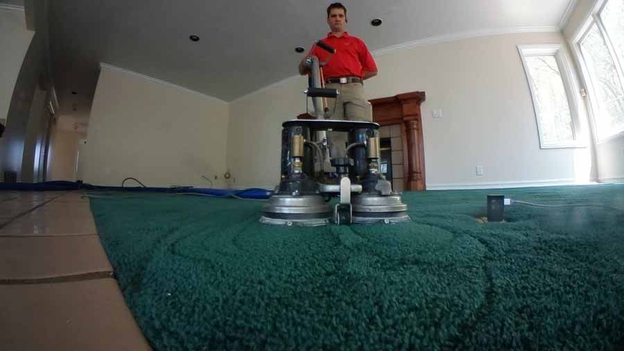 A man is cleaning a green carpet with a machine in a living room.