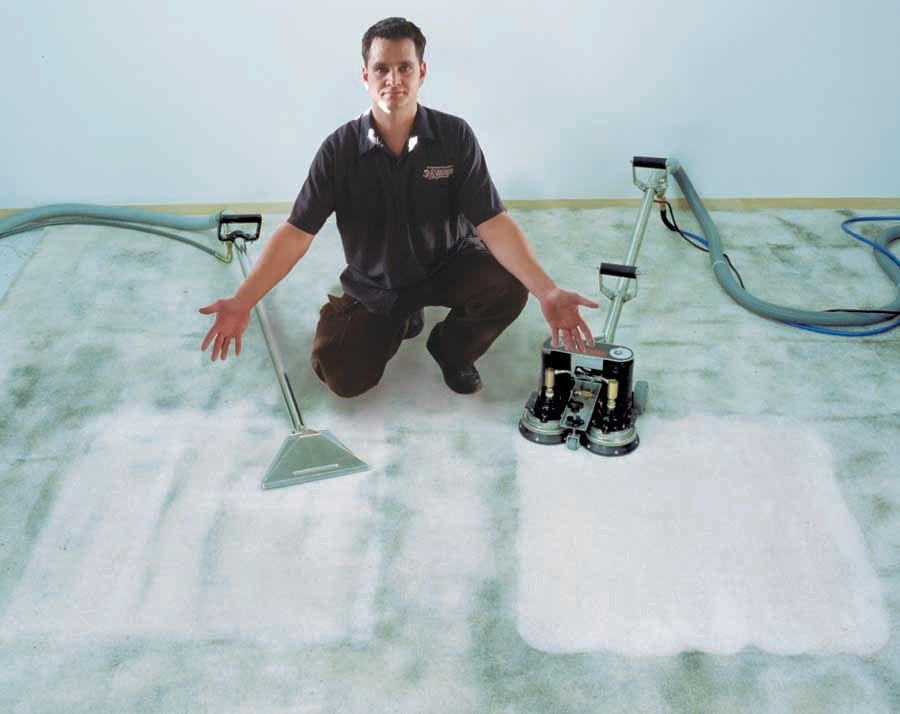 A man is kneeling down next to a vacuum cleaner
