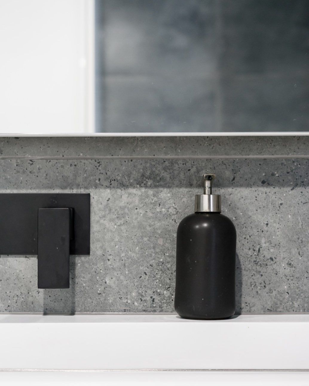 A black soap dispenser is sitting on a bathroom sink next to a mirror.