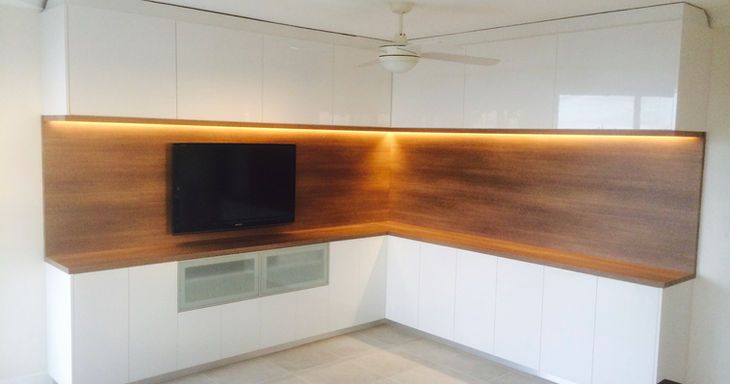 A corner of a room with a tv on the wall and a ceiling fan.