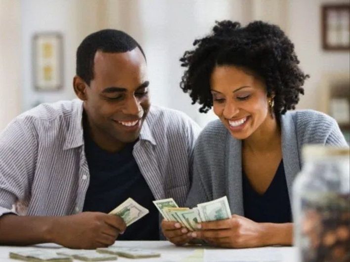 Couple counting money together, smiling, at a table.