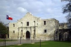 A large stone building with a texas flag flying in front of it.