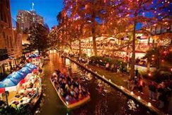 A group of people are riding a boat down a river decorated with christmas lights.