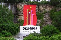 A sign for six flags fiesta texas is in front of a waterfall.