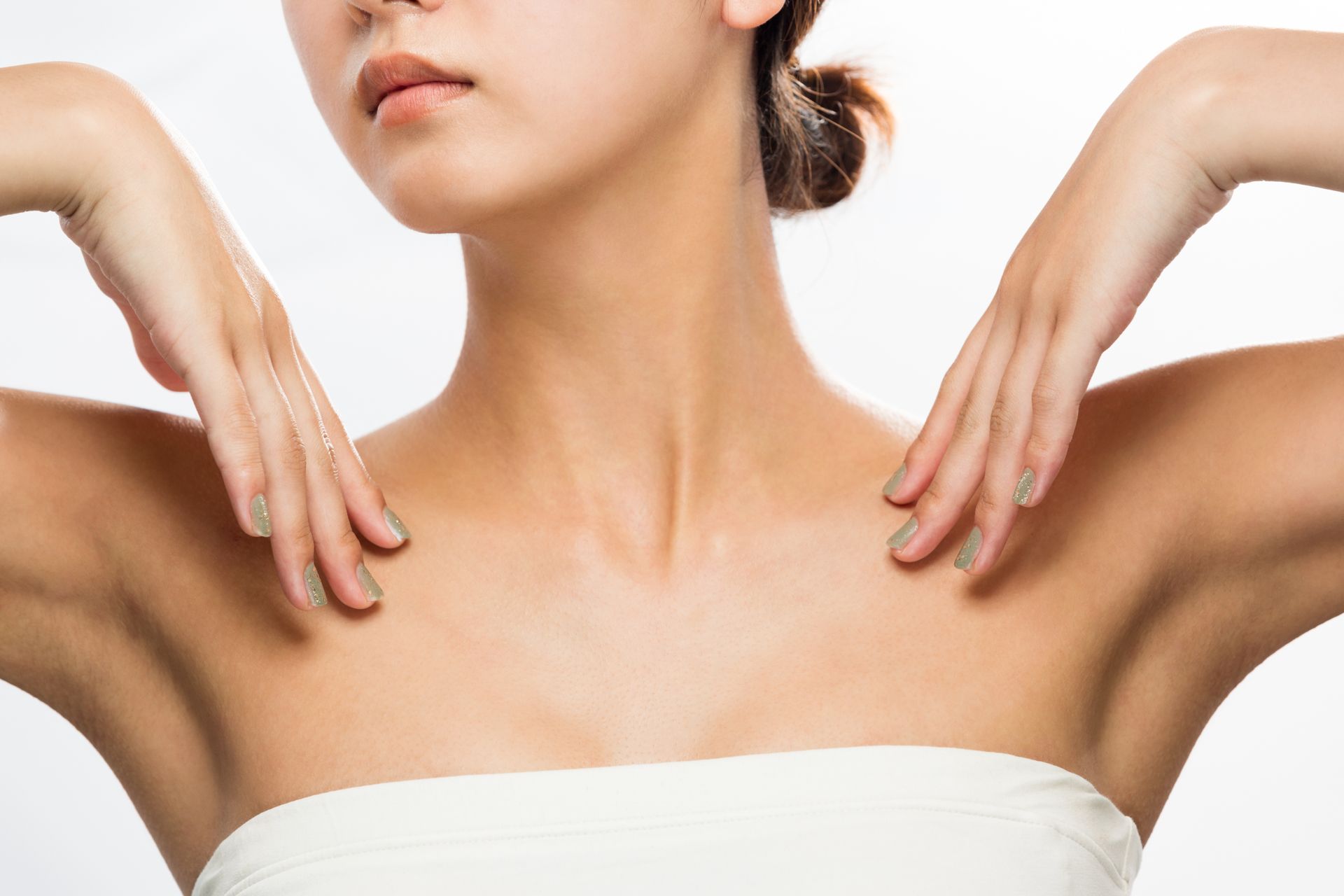 Woman's bare shoulders and upper chest, hands resting on shoulders, against white background.