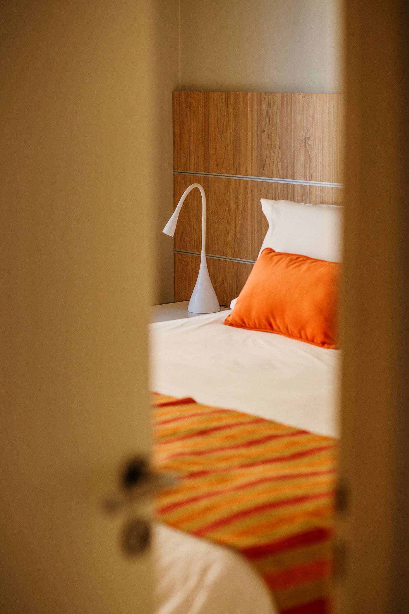 Bed with orange and striped bedding, visible through an open door.