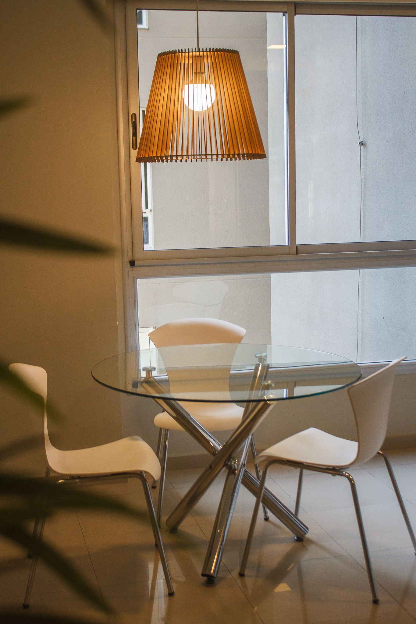 Dining table with three white chairs, under a leopard-print lampshade. Window in the background.