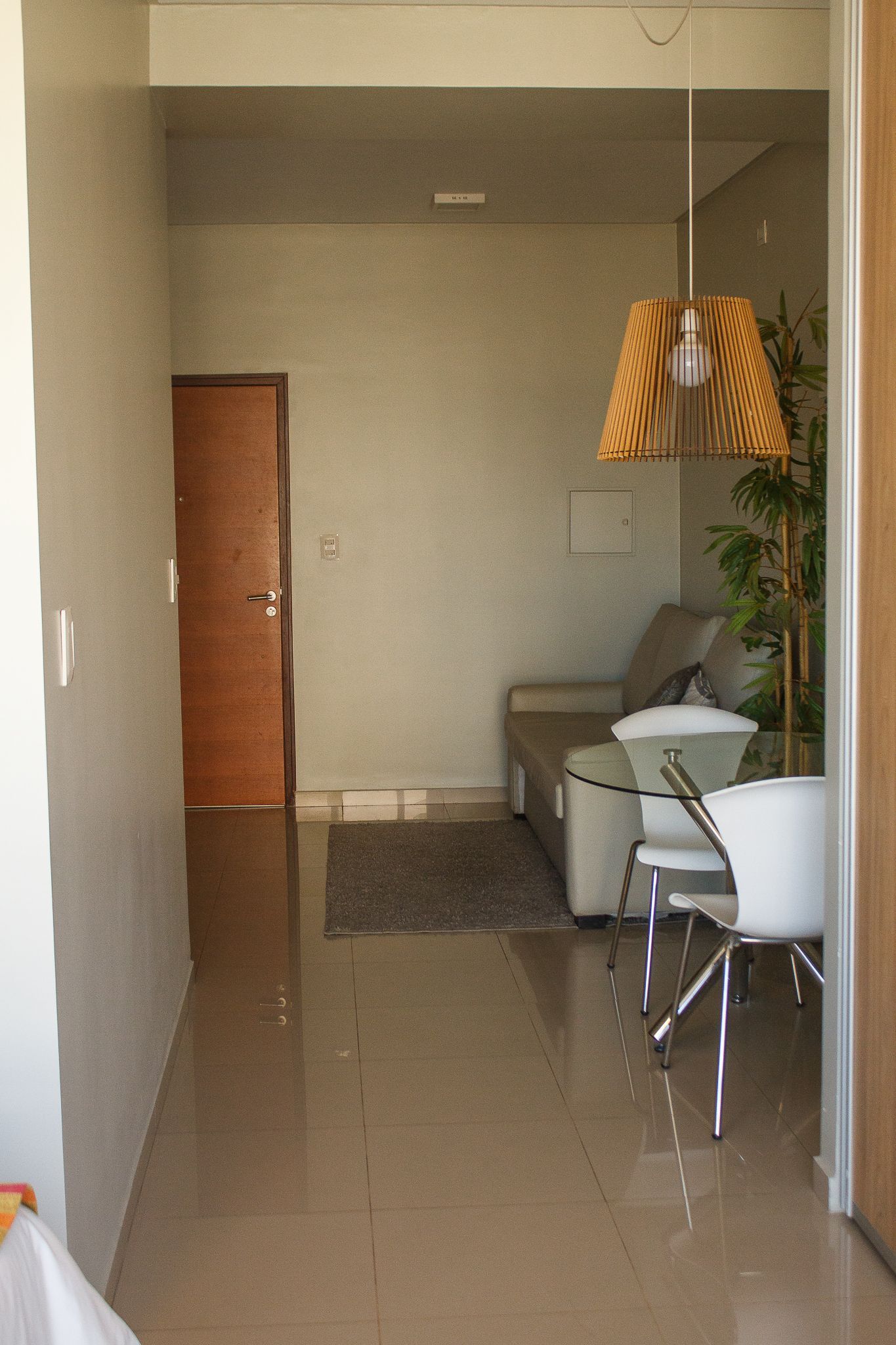 Narrow hallway leading to a small living area. Beige walls, wood door, sofa, lamp, and white chairs.