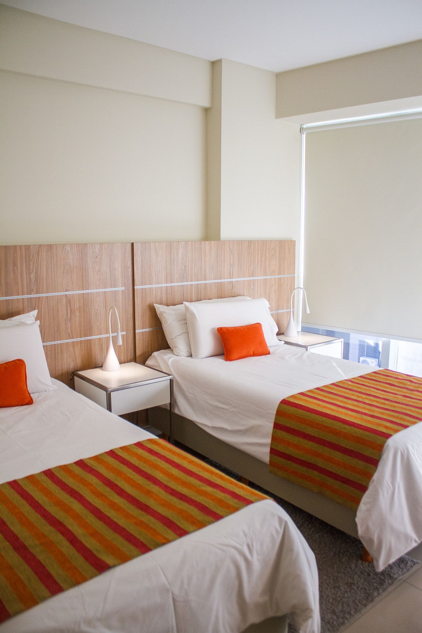 Two twin beds with orange bed runners and pillows in a hotel room.