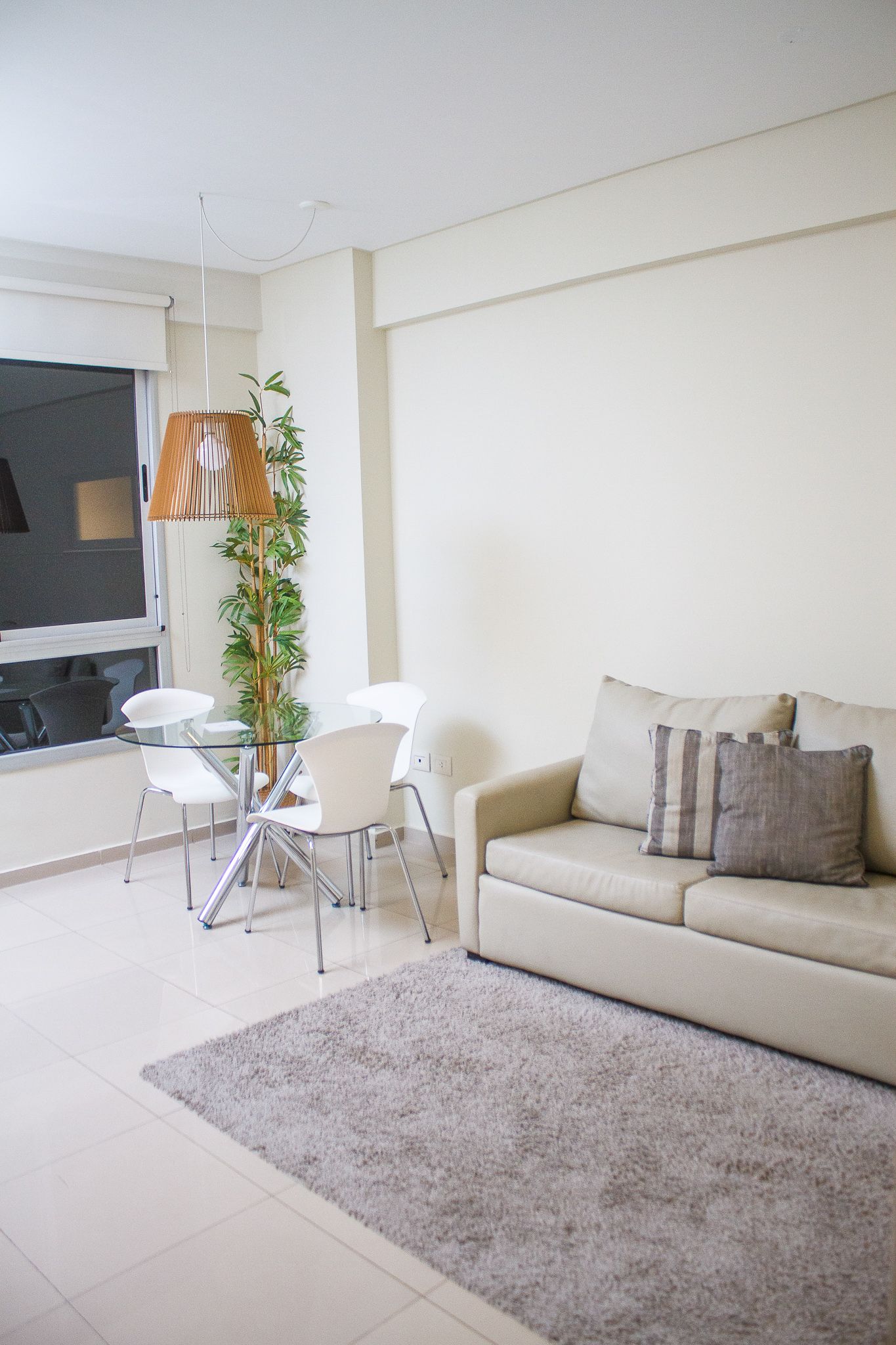 Living room with beige sofa, gray rug, white chairs around a table, and large window.