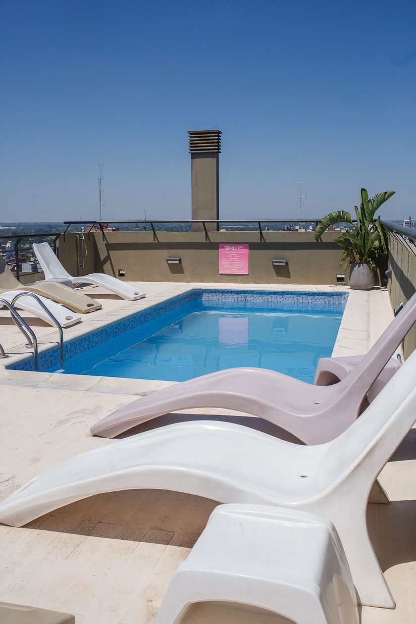 Rooftop pool with two lounge chairs, clear blue water, and a tall chimney. Sunny day.