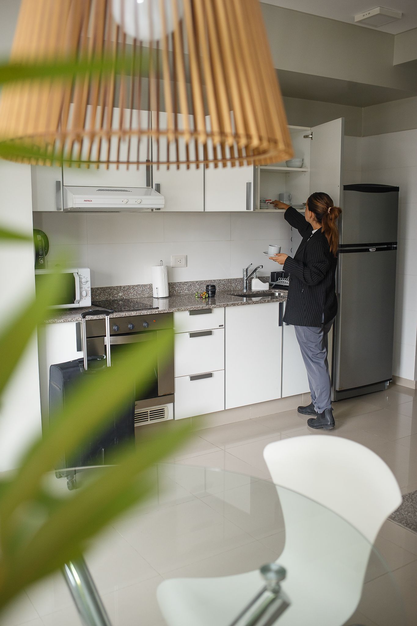 Person opening cabinet in a modern white kitchen, preparing food. Refrigerator visible.