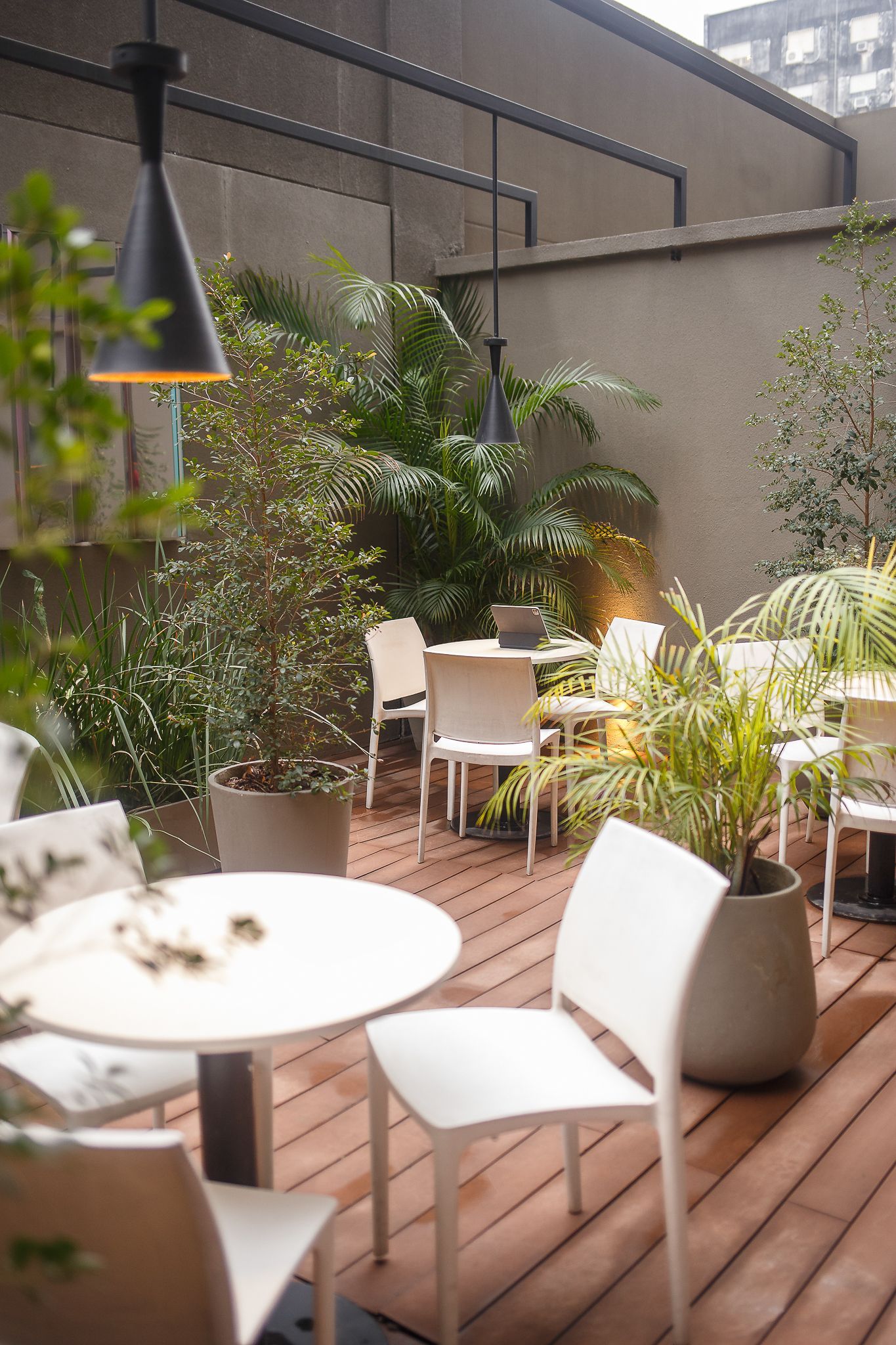Outdoor patio with white tables and chairs surrounded by greenery; wooden deck and neutral-colored walls.