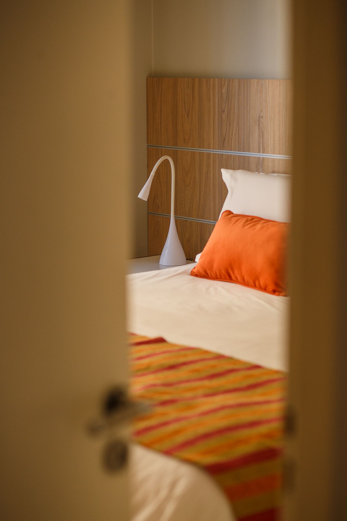 Bedroom interior with bed, orange accents, and lamp.