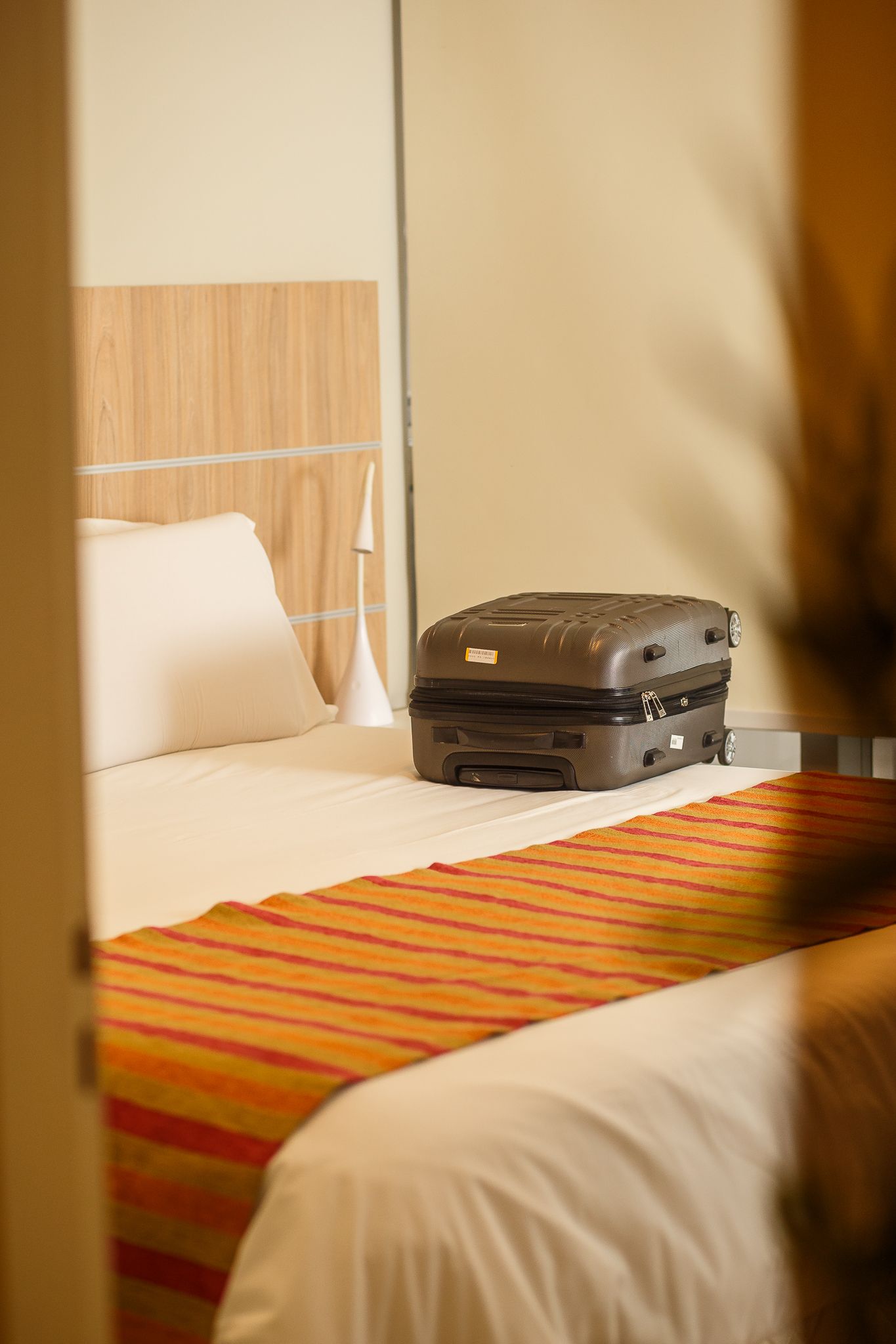 Brown suitcase on a bed in a hotel room with orange bed runner.