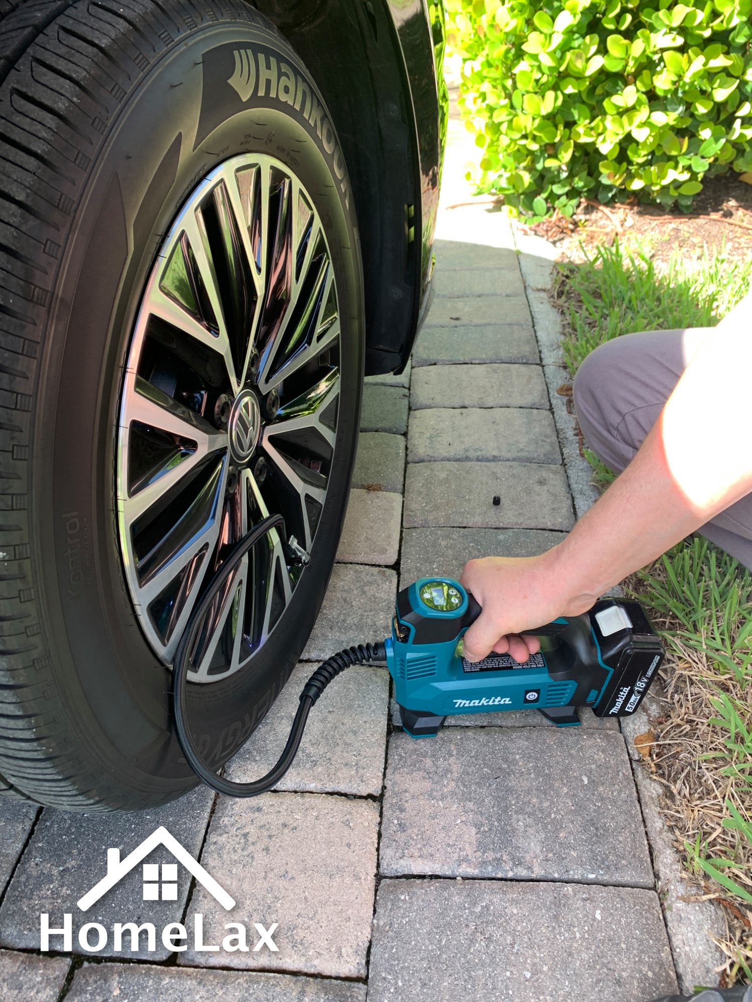 A person is pumping air into a car tire on a sidewalk.