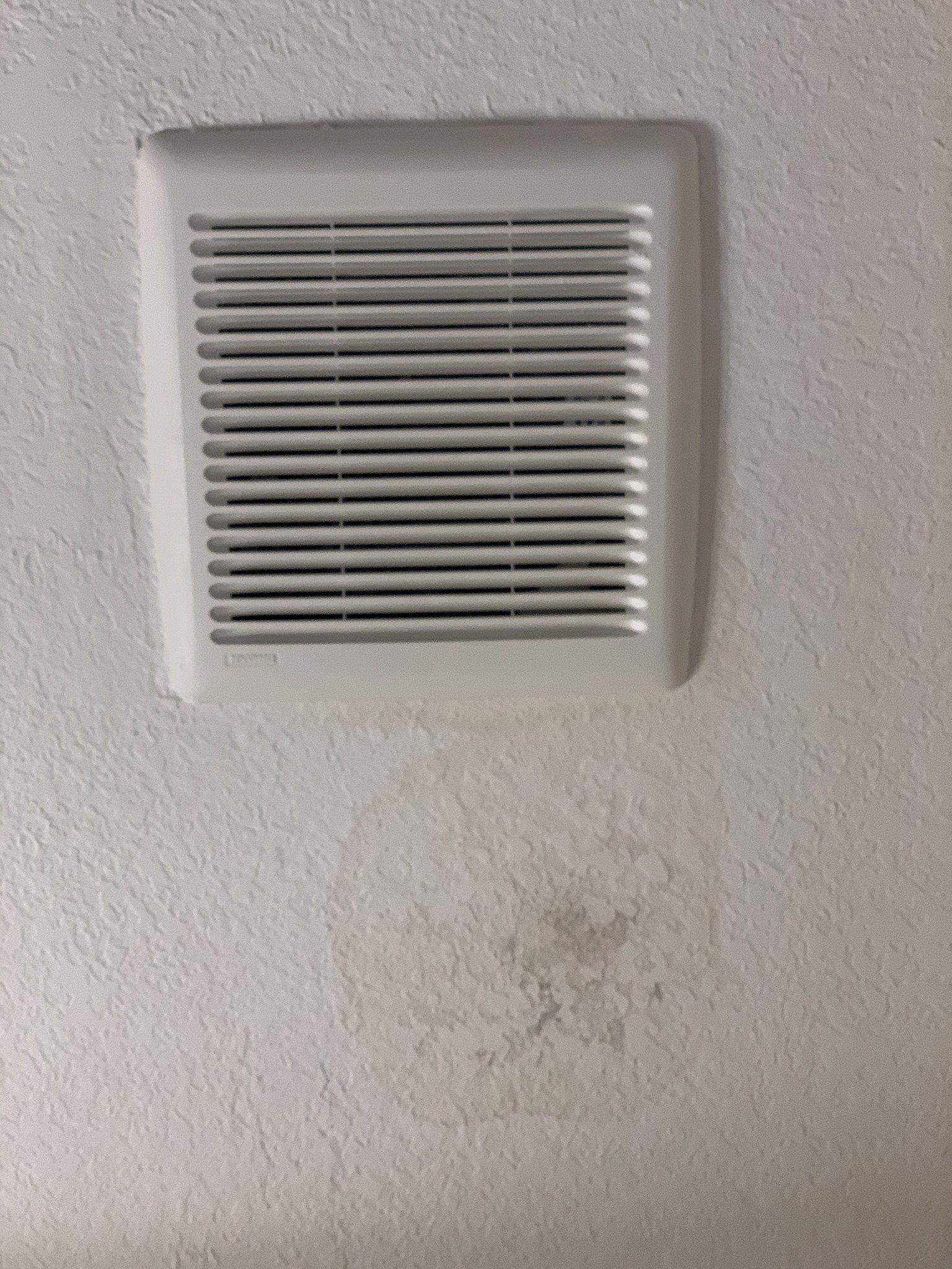 A white air vent is hanging from the ceiling on a white wall.