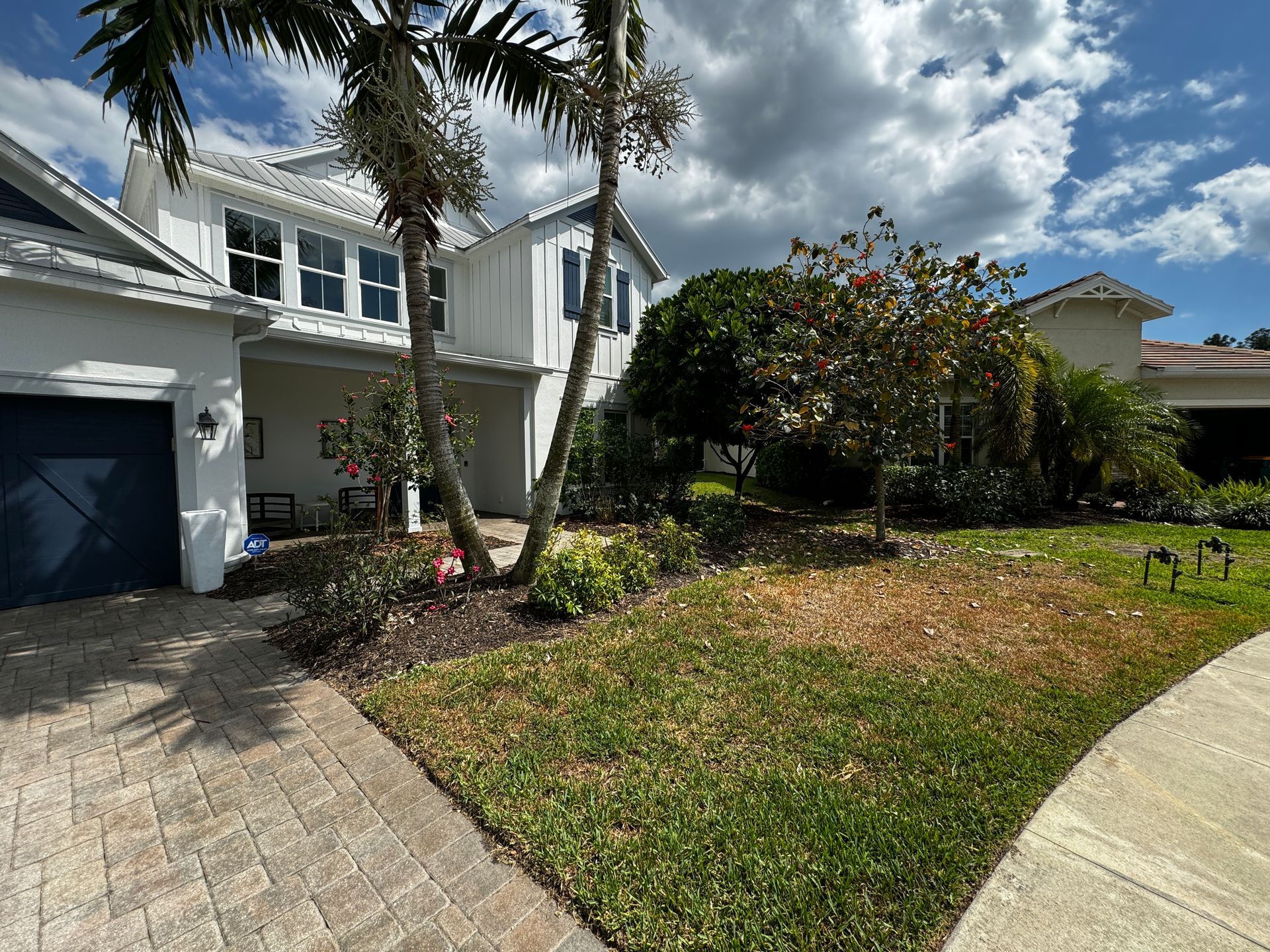 A white house with a blue garage door and a palm tree in front of it.
