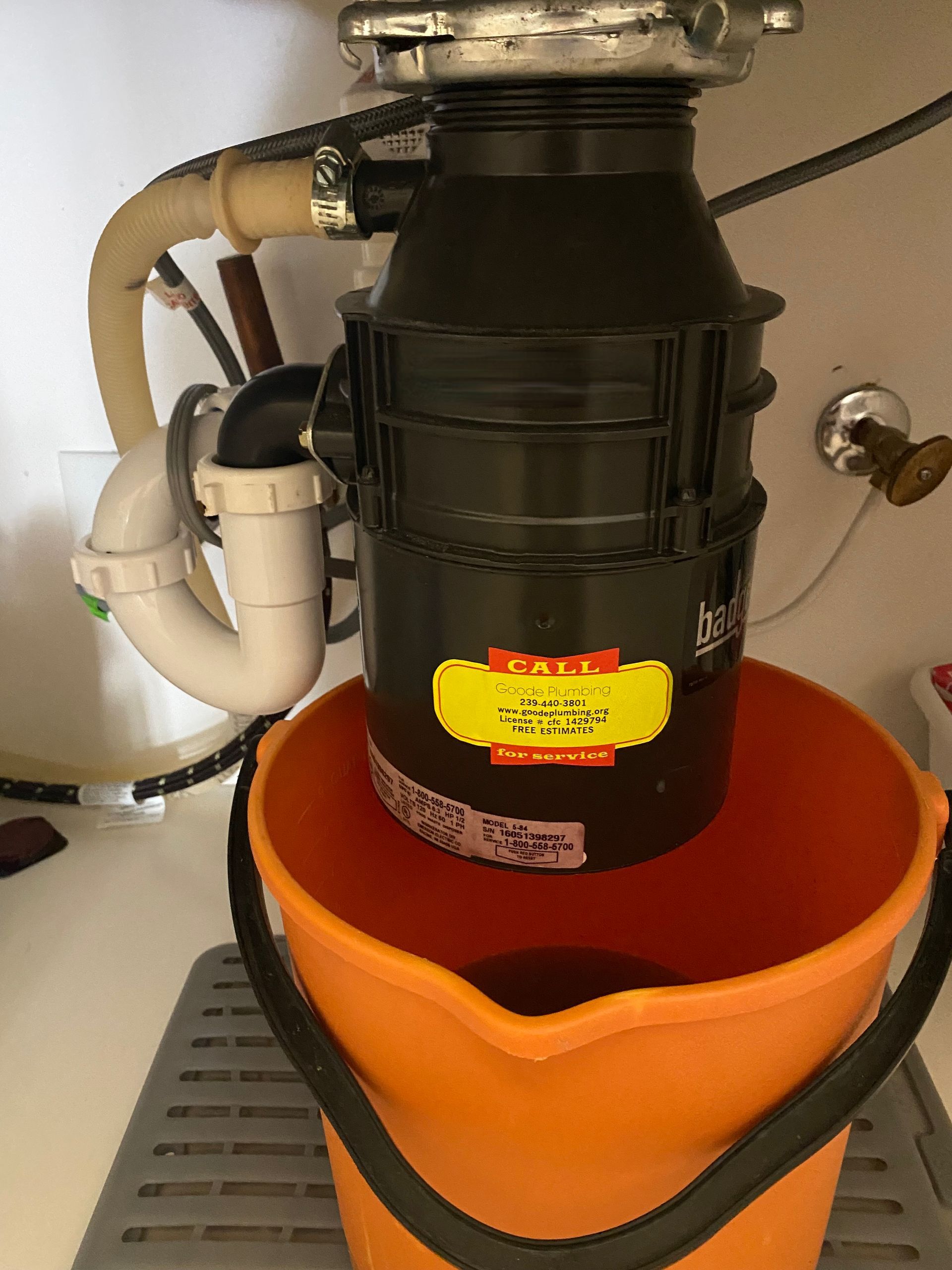 An orange bucket is sitting next to a garbage disposal under a sink.