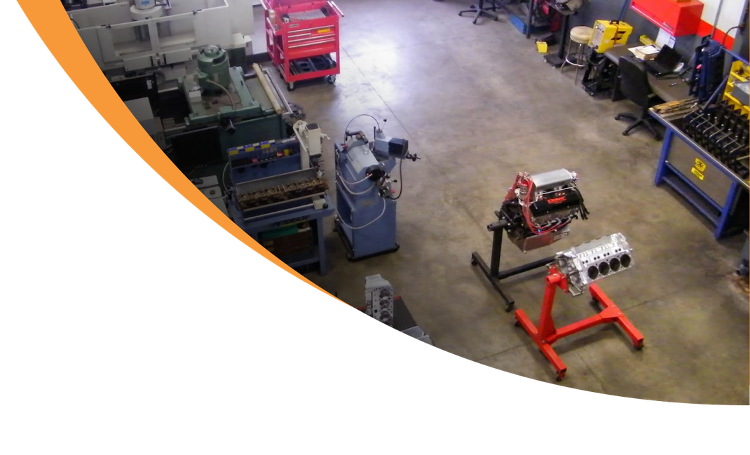 A well-lit auto repair shop with engine parts displayed and tools, with an orange curve in the upper left corner. | Don's Performance Corner