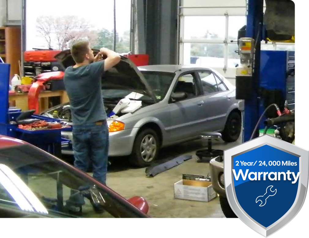 Mechanic working on car in a garage with 2-year/24,000-mile warranty badge. | Don's Performance Corner