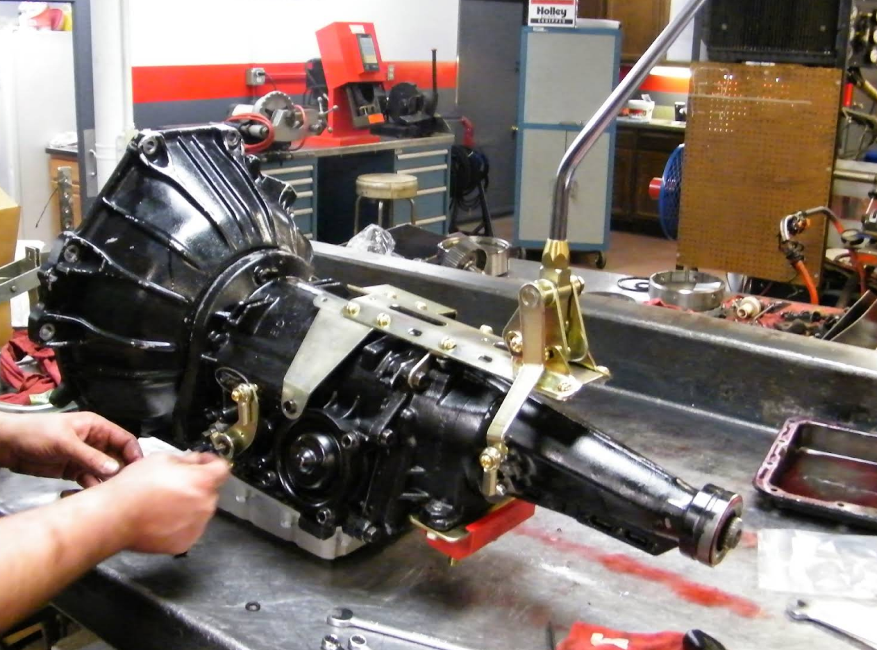 Black automatic transmission on a workbench; person working on the side. | Don's Performance Corner