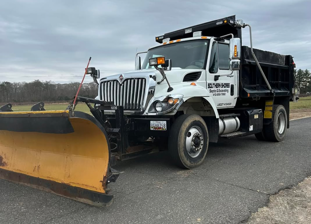 A dump truck with a snow plow attached to it is parked on the side of the road.