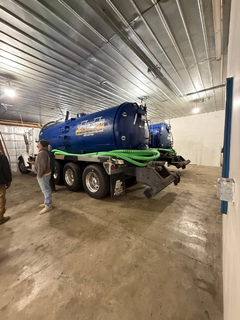 Blue septic tank truck inside a building, two people standing near the truck.
