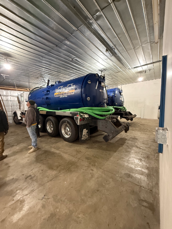 Blue septic tank truck inside a building, two people standing near the truck.