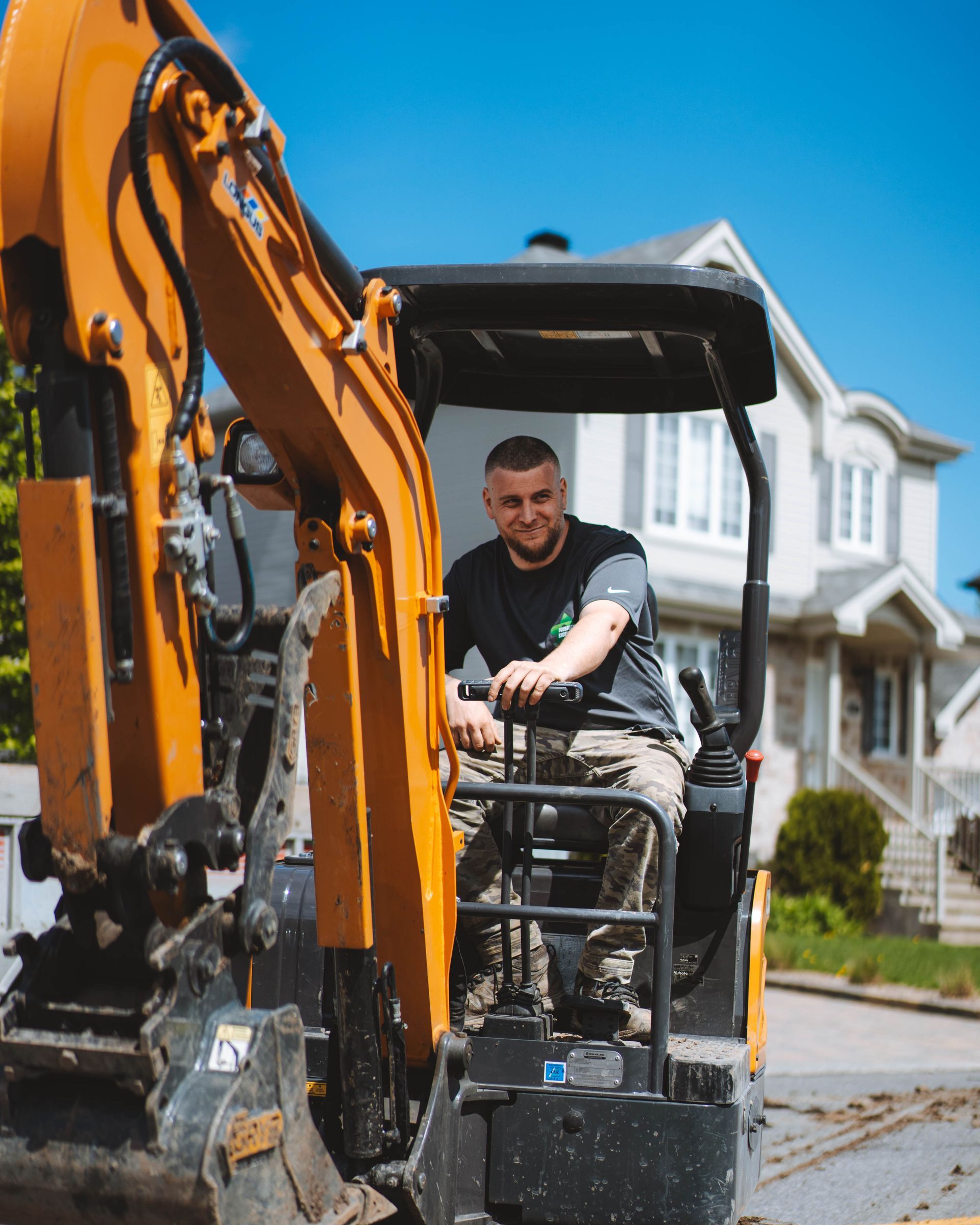 Homme dans une excavatrice, souriant, devant une maison.