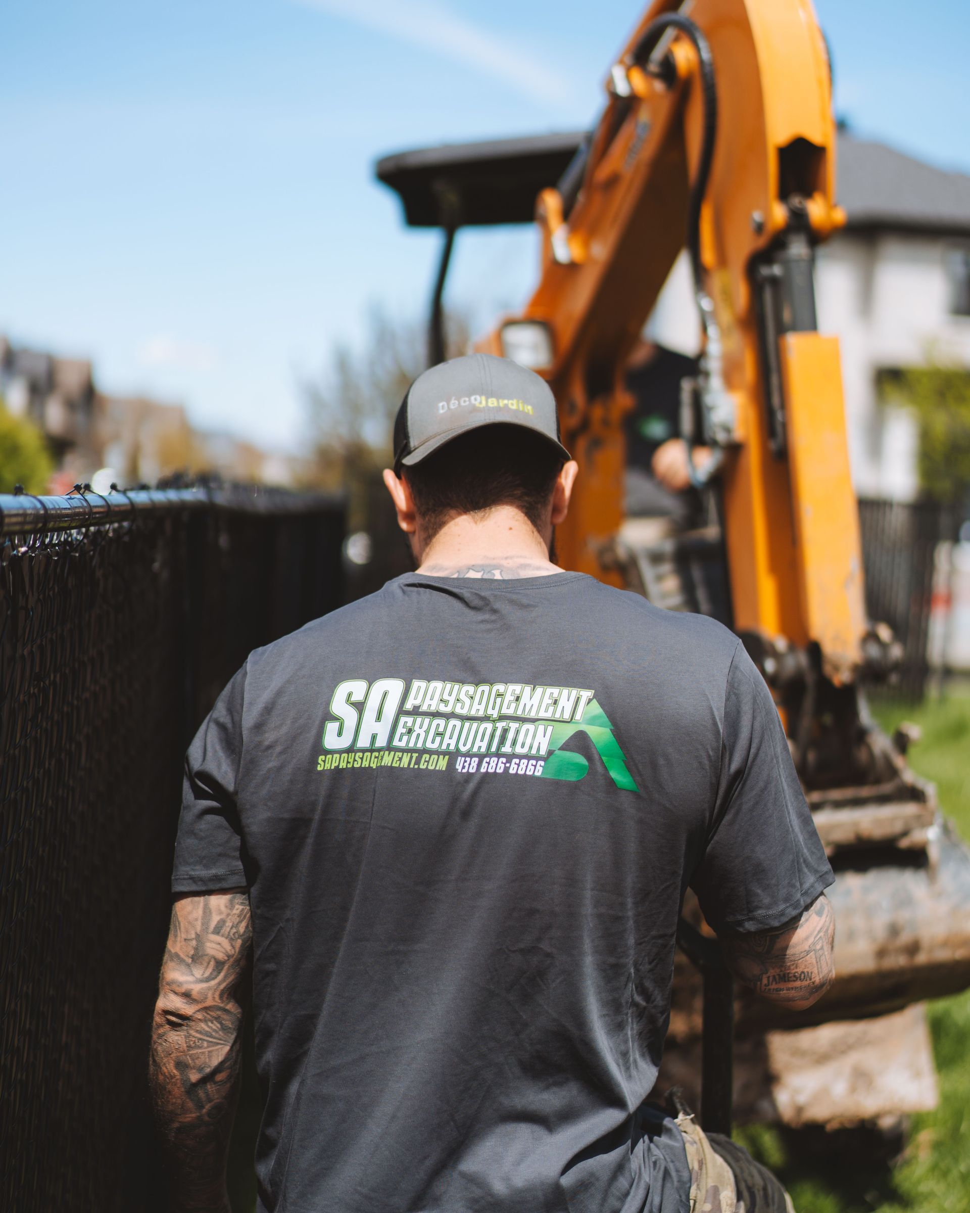 Un homme en t-shirt gris avec le logo « SA Abatement Excavation » utilise une excavatrice près d'une clôture.