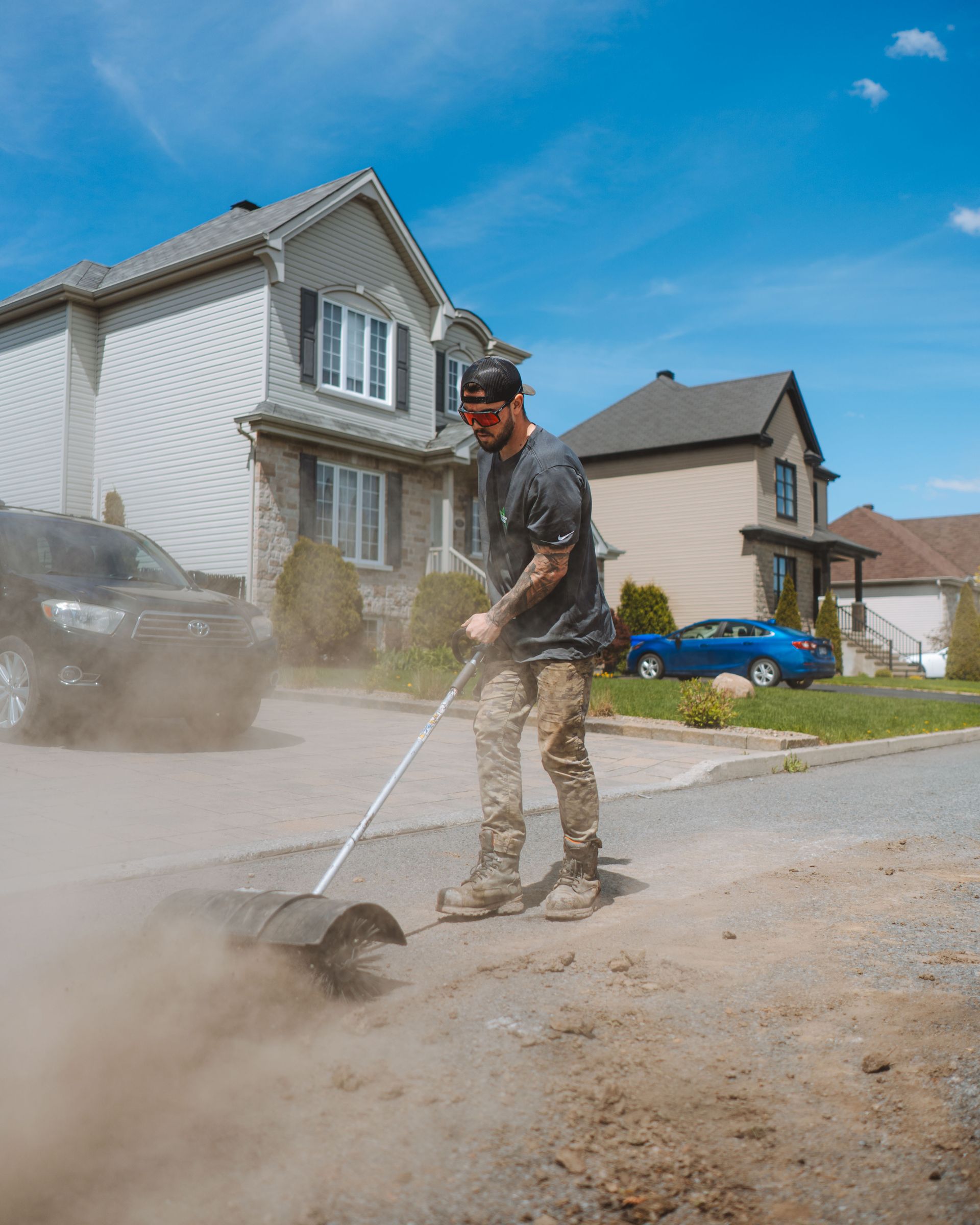 Un homme balaye une allée de gravier près des maisons par une journée ensoleillée.