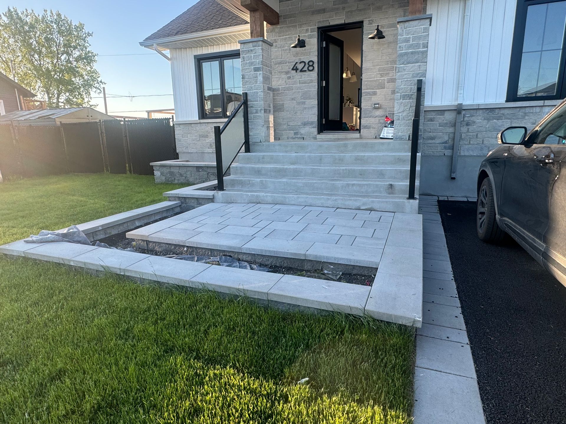 Une maison moderne avec façade en pierre, marches menant à la porte d'entrée, balustrades noires et allée pavée.