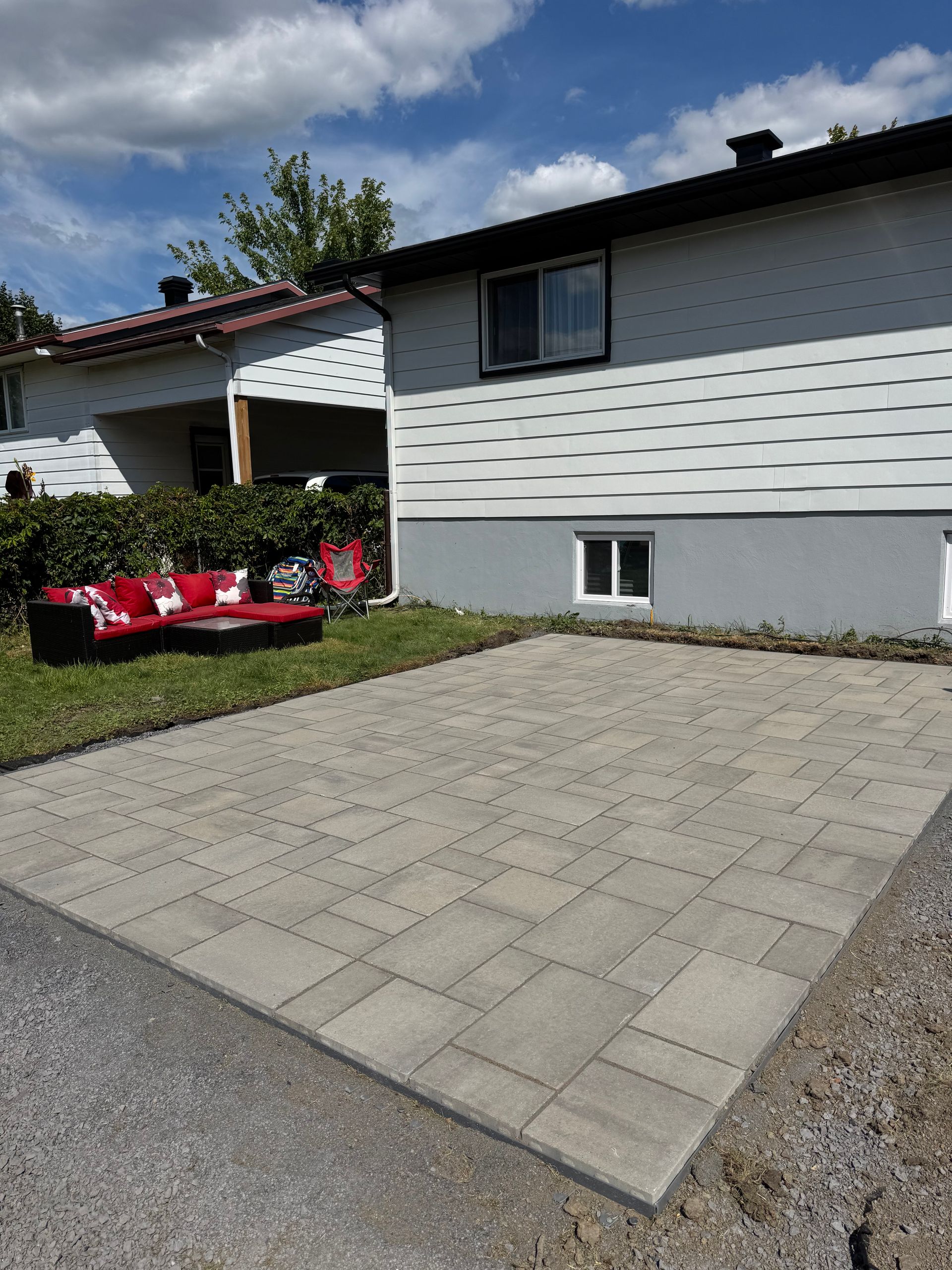 Un patio en pavés gris devant une maison à deux étages avec un canapé rouge sur la pelouse.