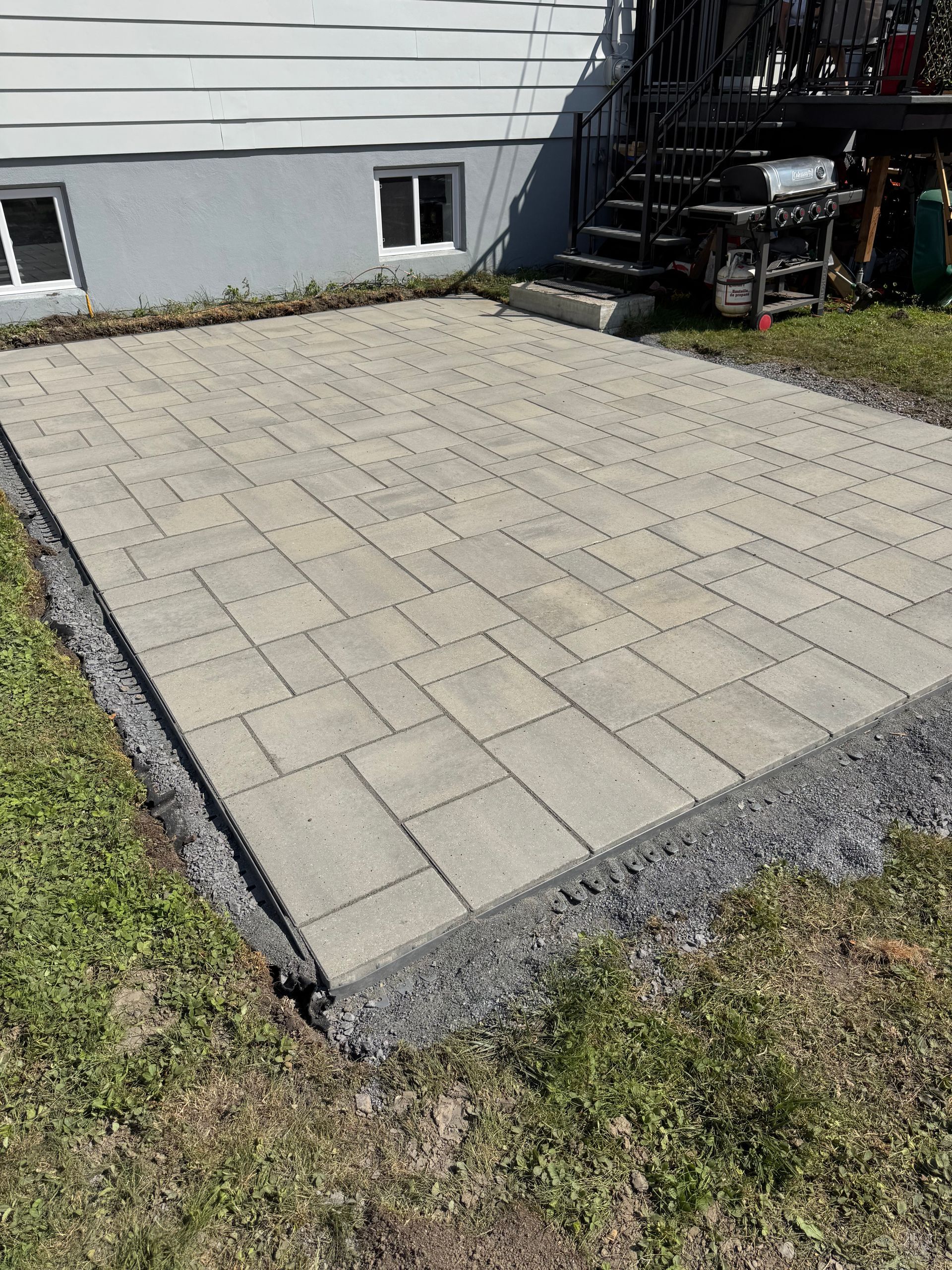 Un patio pavé de pavés gris à côté d'un bâtiment, entouré de gravier et d'herbe.