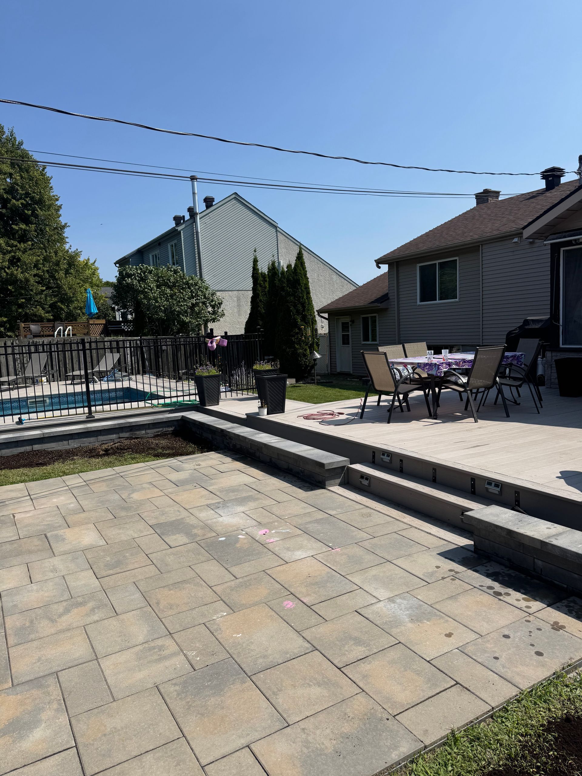 Patio avec pavés, marches et ensemble de salle à manger extérieur; piscine en arrière-plan, journée ensoleillée.
