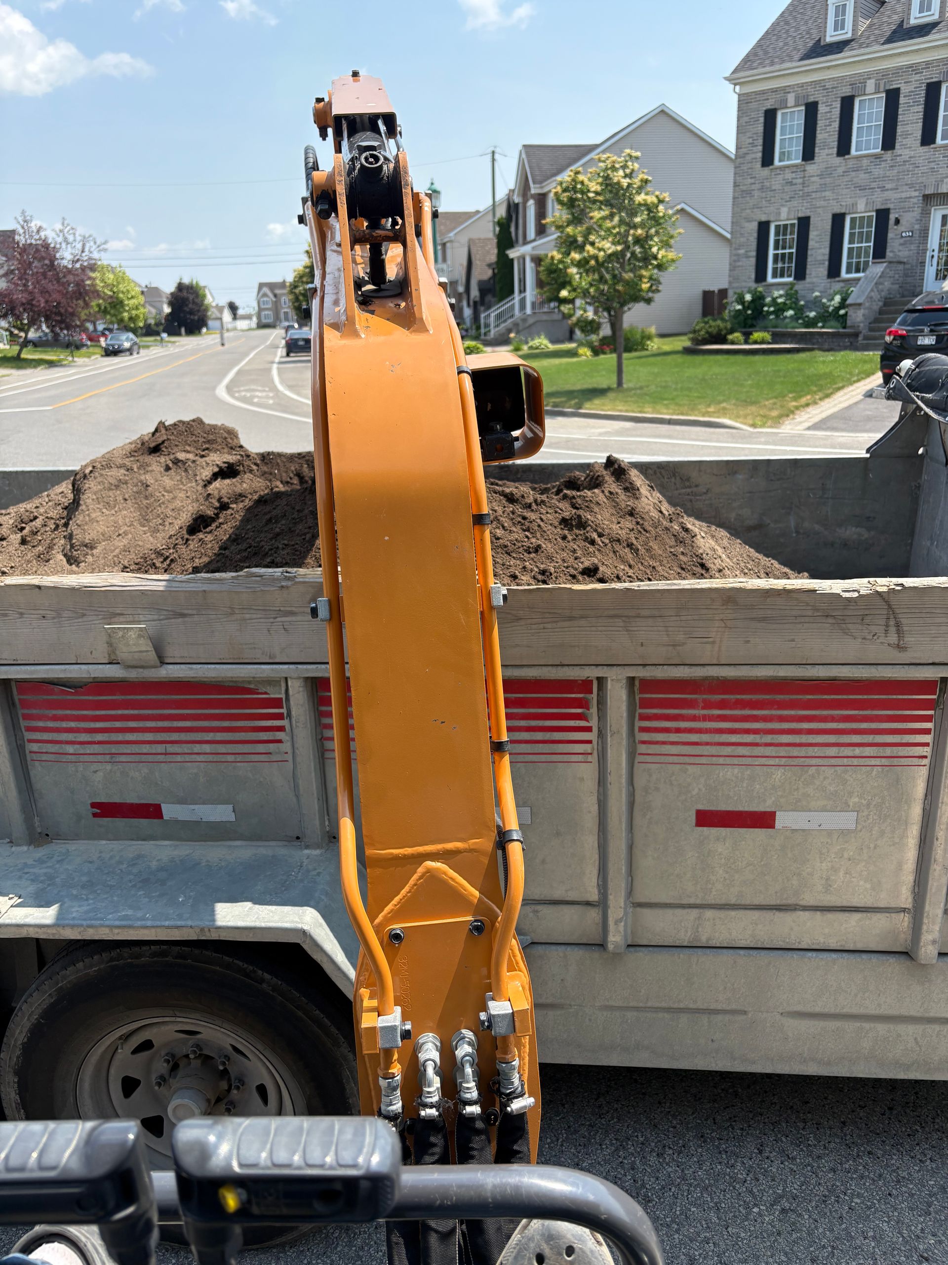 Une excavatrice orange chargeant de la terre brune dans un camion à benne basculante par une journée ensoleillée.