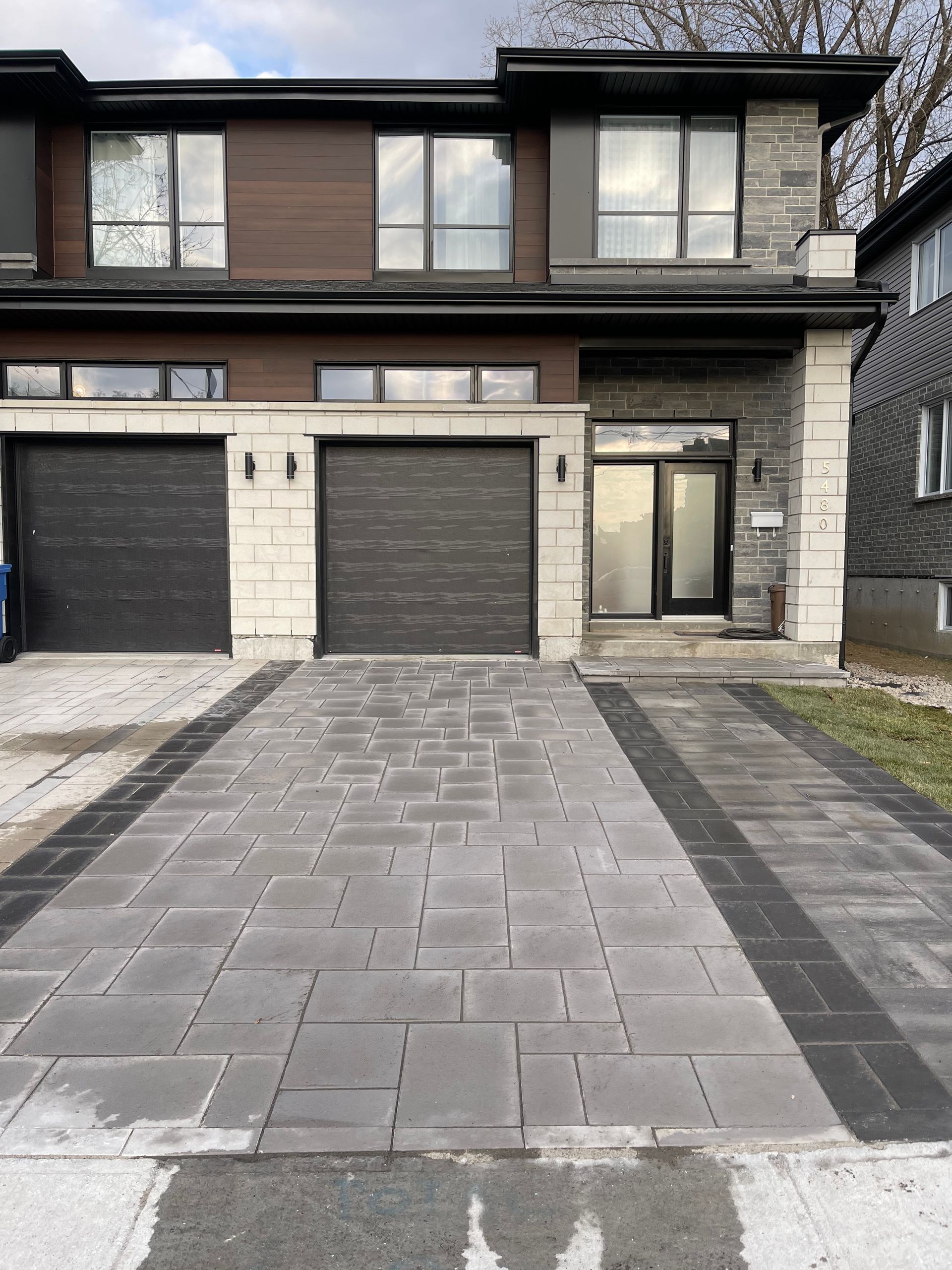 Maison de ville moderne avec allée pavée grise et portes de garage noires.