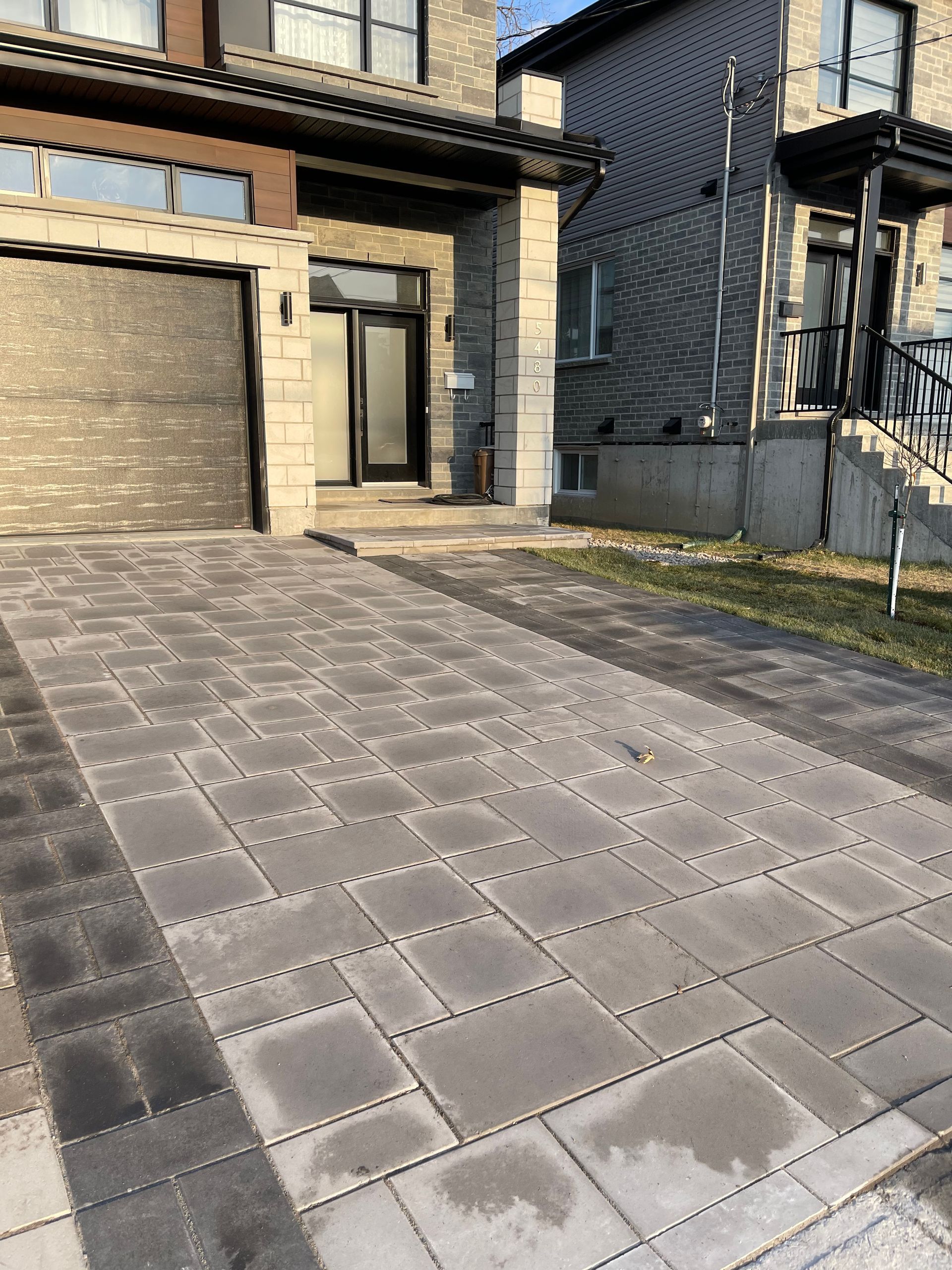 Allée pavée de blocs rectangulaires gris menant à une maison avec porte de garage.