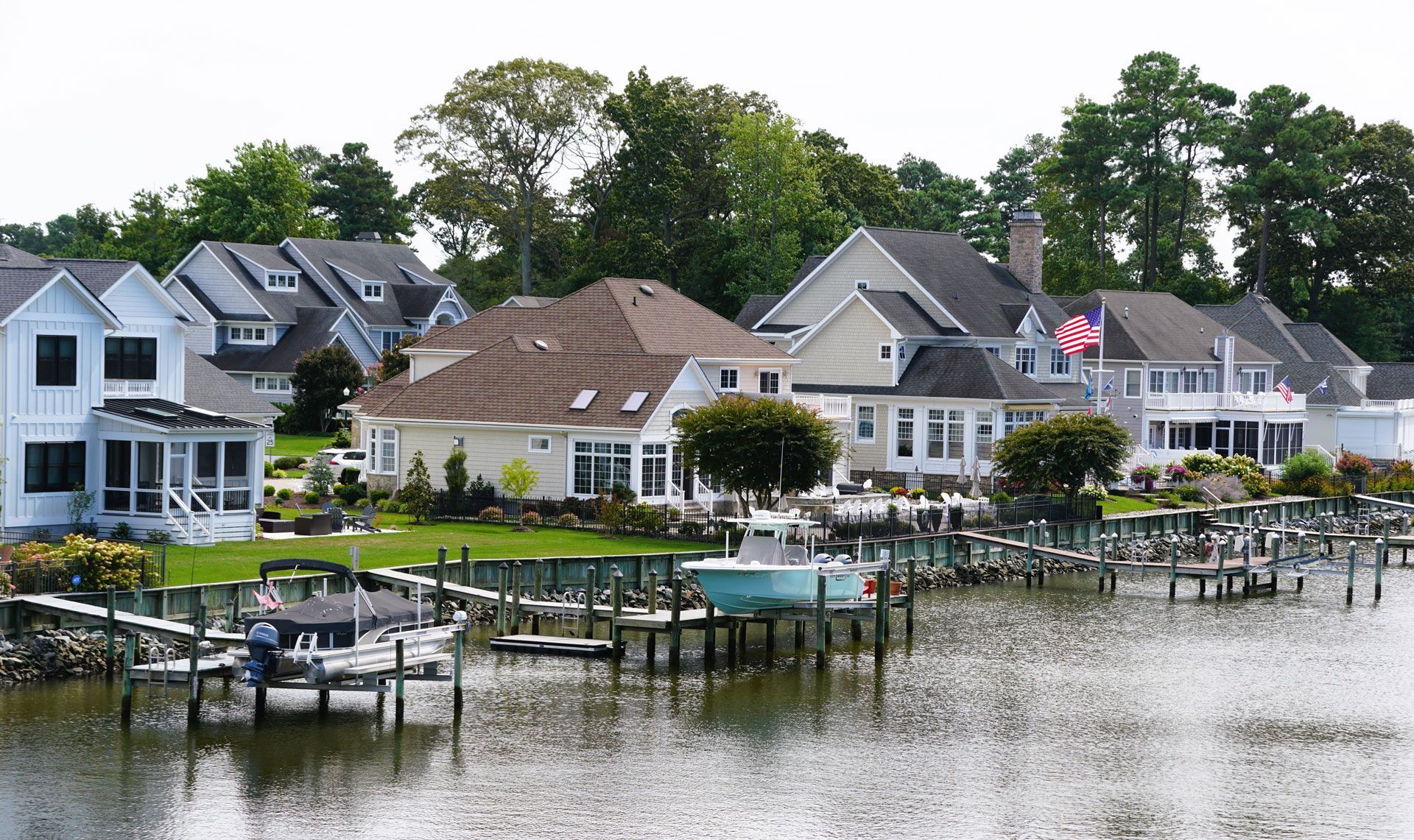 Waterfront homes with docks and boats along a calm waterway, under a partly cloudy sky.