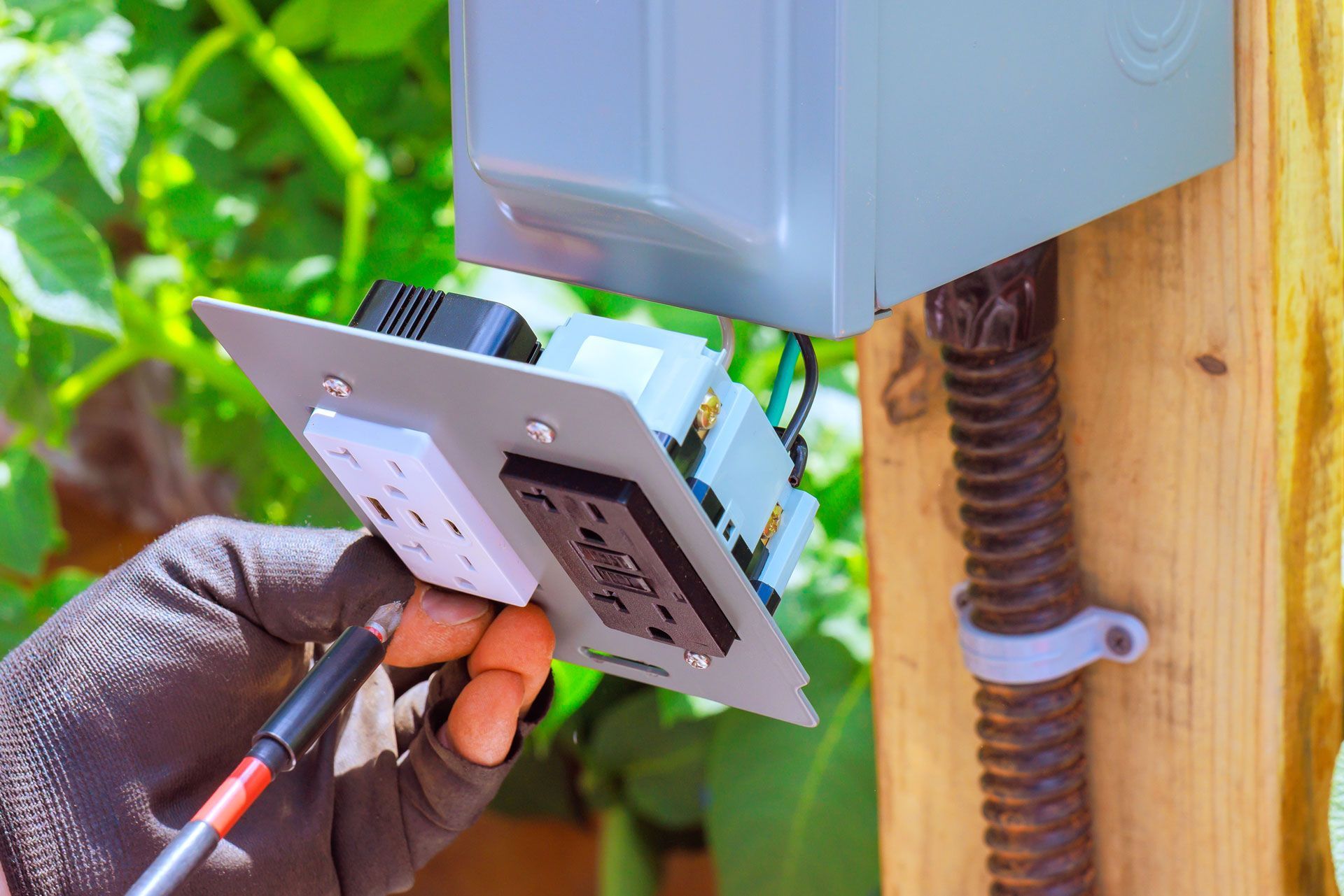 Person with gloved hand wiring an electrical outlet box on wooden post.