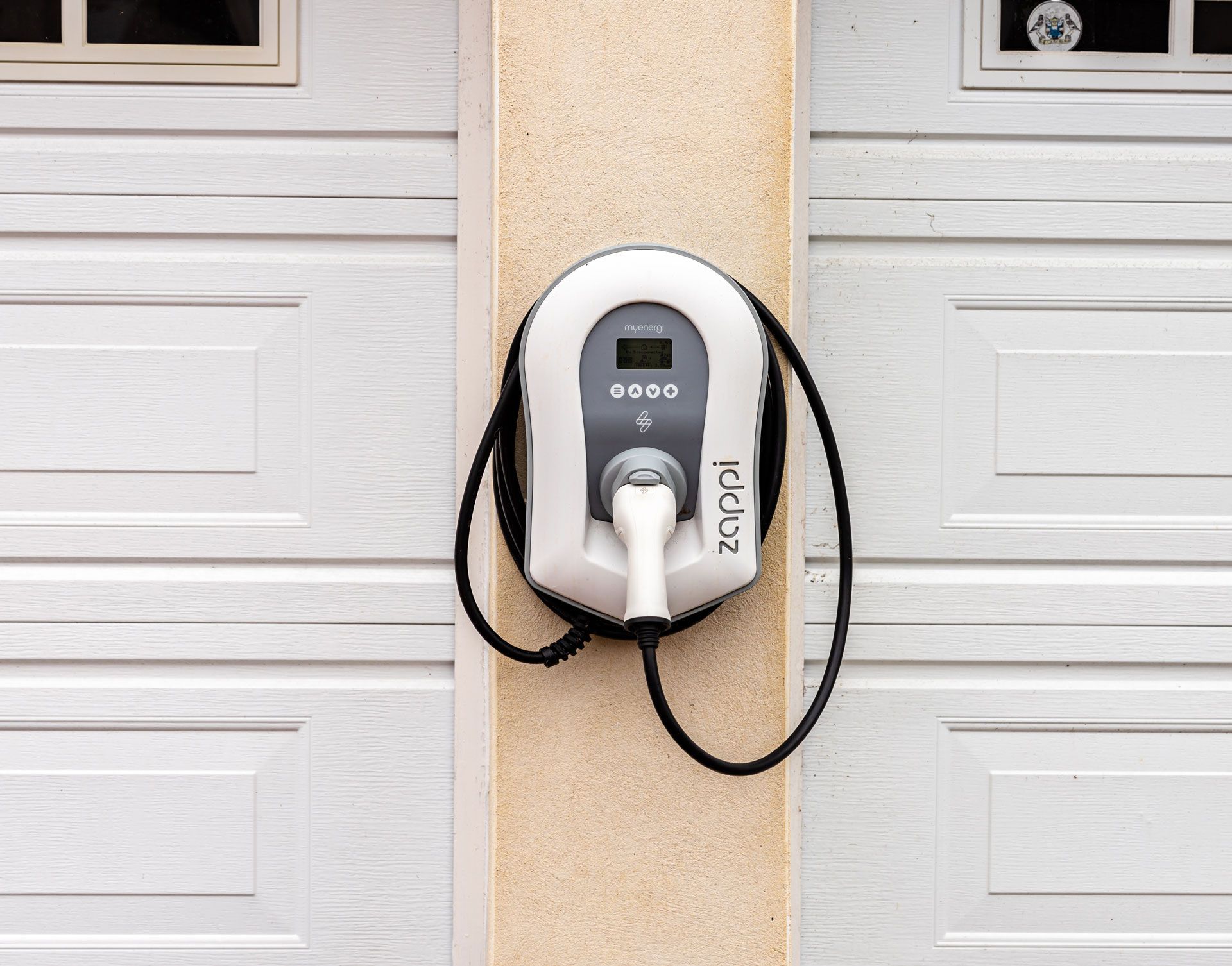An electric car charger is attached to the side of a garage door.