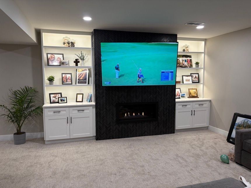 Built-in cabinets frame a TV and fireplace, with shelves displaying photos and decor. A golf game is on the television screen.