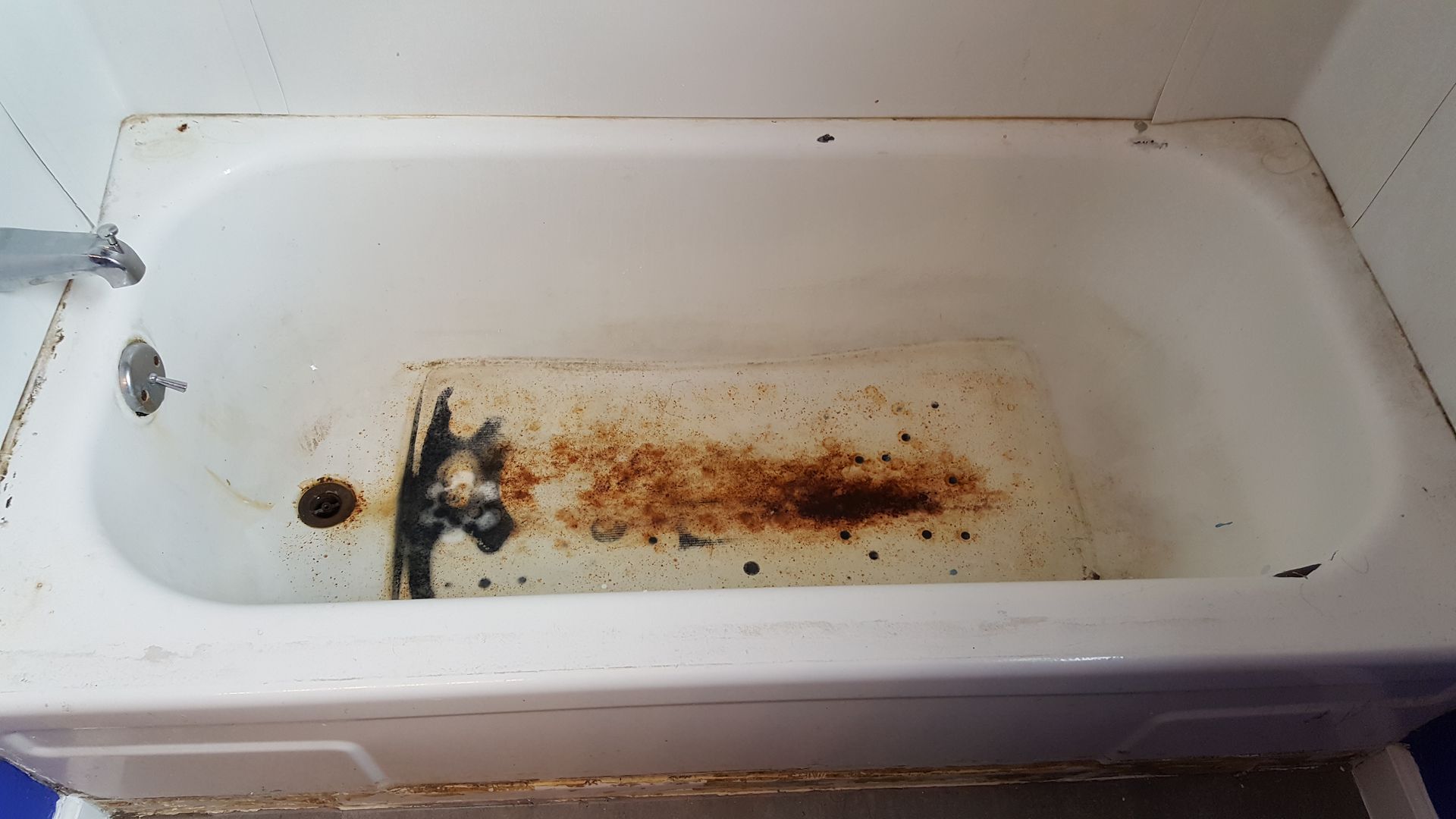 a white bathtub with a rusty bottom in a bathroom .