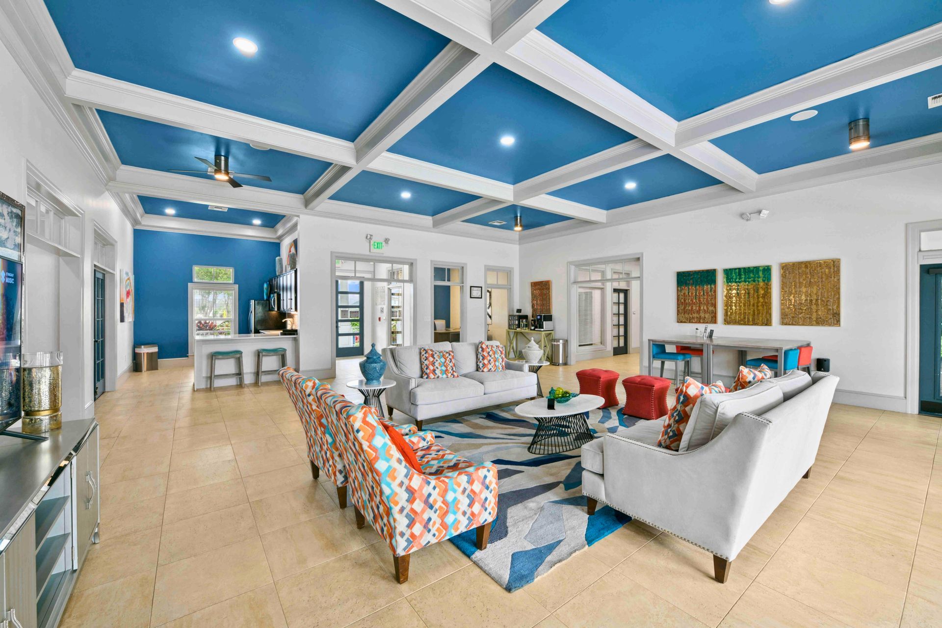 Spacious lobby with blue ceiling and white beams, couches, patterned chairs, and a central rug.