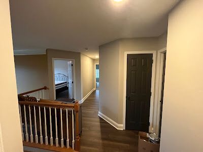 Hallway with dark wood floor, tan walls, white trim, and black door. Stairs with wood railing are on the left.