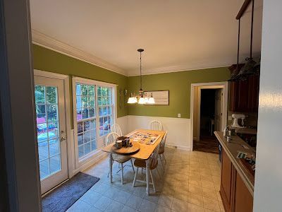 Dining room with a table, chairs, and green walls, next to French doors and a doorway.