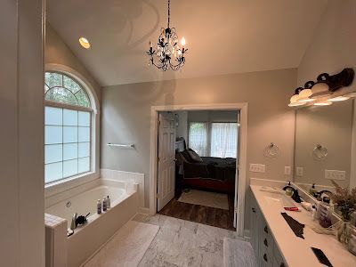 Bathroom with a jacuzzi tub, vanity, and doorway to a bedroom. Neutral walls, chandelier, and frosted arched window.